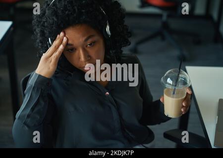 Müde multirassische Frau sitzt am Arbeitsplatz und leidet unter Kopfschmerzen Stockfoto