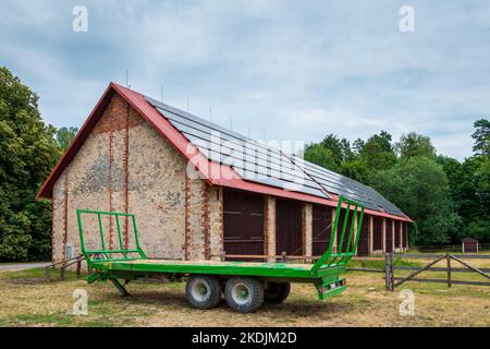 Green Farm Anhänger vor einer großen Scheune geparkt. Solarpaneele auf dem Dach der Scheune installiert Stockfoto