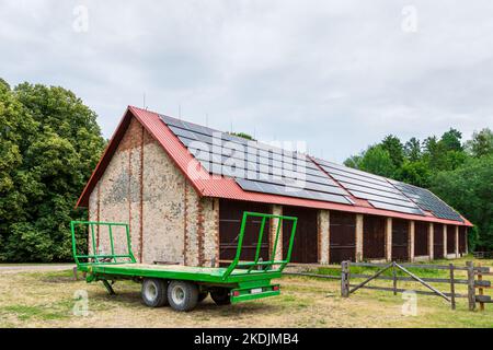 Green Farm Anhänger vor einer großen Scheune geparkt. Solarpaneele auf dem Dach der Scheune installiert Stockfoto