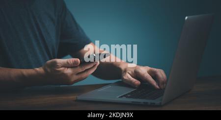 Mann hält Smartphone immer Nachricht mit Bestätigung, die Transaktion, Übertragung, Synchronisierung von Daten über bluetooth auf Laptop-Computer. Stockfoto
