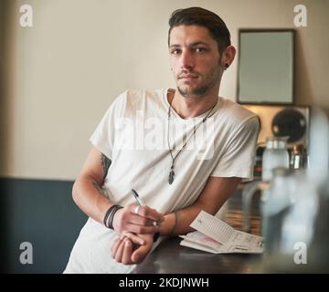 Wenn Sie es trinken können, kann er es mischen. Porträt eines ernsthaften jungen Barkeepers, der sich an der Theke lehnt. Stockfoto