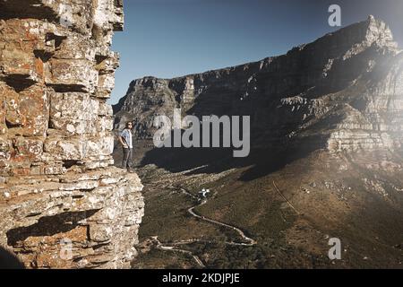 Was für eine Aussicht. Ein junger Mann, der am Rande einer Bergklippe mit Blick auf ein Tal steht. Stockfoto