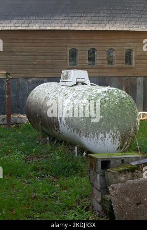 Ein Gastank wird in einem Garten aufgestellt, er ist mit Flechtenmoos bedeckt, er ist von Baustoffen umgeben. Stockfoto