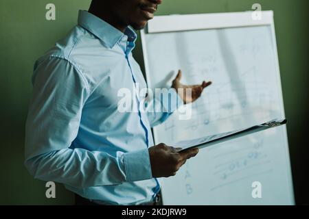 Zugeschnittene Aufnahme eines selbstbewussten Musiklehrers mit Zwischenablage, die neben dem Whiteboard mit Musiknoten steht und dem Publikum erklärt Stockfoto