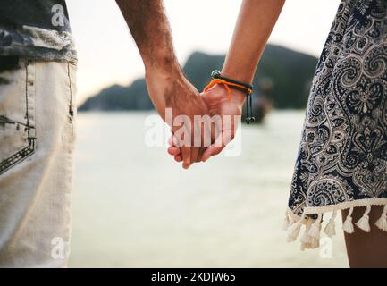 Überall ist perfekt, solange man Hand in Hand war. Nahaufnahme eines jungen Paares, das die Hände am Strand hält. Stockfoto