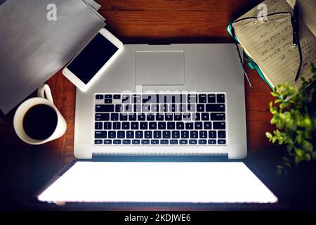 Bereit, online zu gehen. High-Angle-Aufnahme eines Laptops und anderer Gegenstände, die am Abend auf einem Schreibtisch sitzen. Stockfoto