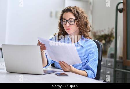 Junge Geschäftsführerin mit Dokumenten, die mit einem Laptop im Büro arbeiten. Stockfoto