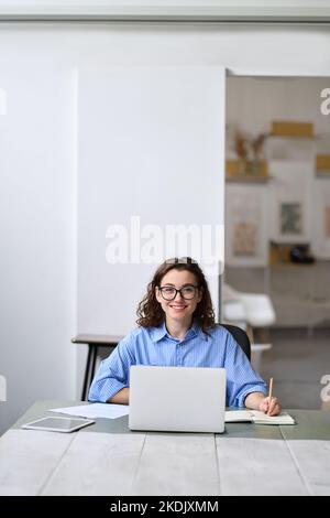 Junge glückliche Geschäftsfrau Student sitzt am Schreibtisch mit Laptop. Hochformat Stockfoto