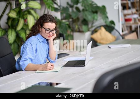 Junge Geschäftsfrau oder Studentin, die mit einem Laptop arbeitet oder lernt, Notizen zu machen. Stockfoto