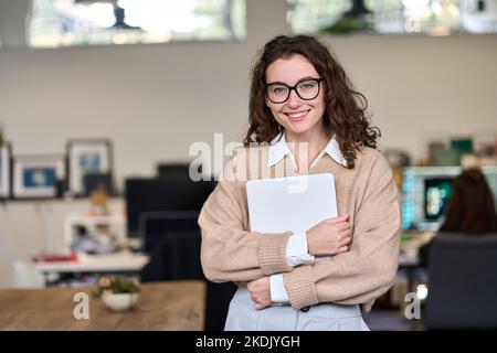 Junge lächelnde Geschäftsfrau, die im Büro steht und die Kamera anschaut. Stockfoto