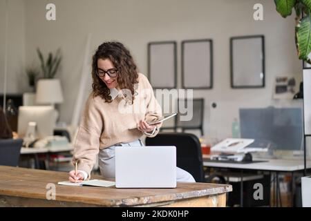 Junge lächelnde, vielbeschäftigte Geschäftsfrau, die im Büro mit einem digitalen Tablet arbeitet. Stockfoto