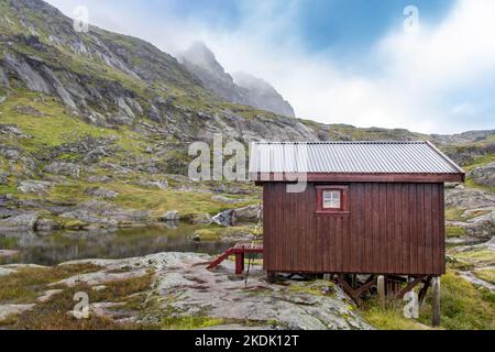 Auf einer einzigen roten Hütte in den Felsen in der Nähe eines kleinen Sees mit wolkenblauem Himmel Stockfoto