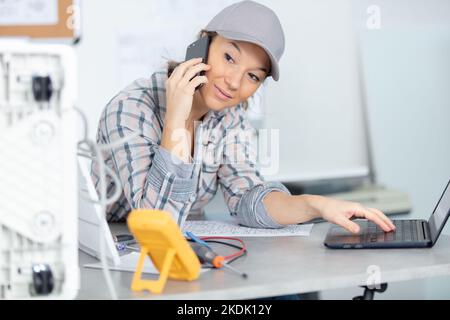 Technikerin mit Laptop und Gespräch auf dem Smartphone Stockfoto