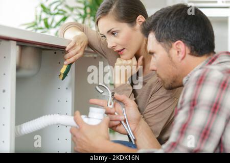 Frau, die den Blick der Arbeiter unter dem Waschbecken beobachtete Stockfoto