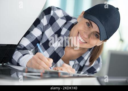 Eine glückliche Frau, die im Büro auf der Zwischenablage schreibt Stockfoto