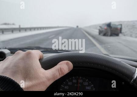 Blick auf die Fahrerhand hinter dem Steuer eines Autos, das an einem angefahrenen Auto vorbeifährt Stockfoto