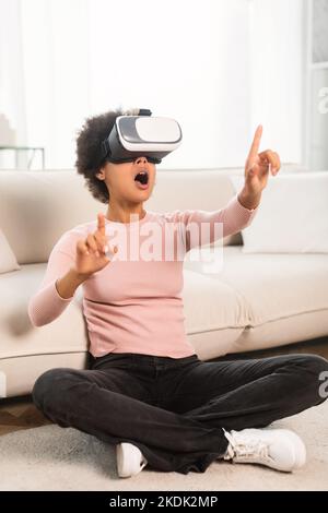 Froh schockiert tausendjährige afroamerikanische Frau mit offenem Mund in vr Brille gestikulierend, sitzen auf dem Boden Stockfoto