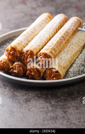 Hausgemachte Waffeln Brötchen mit Karamell und Puderzucker auf dem Teller auf dem Tisch. Vertikal Stockfoto