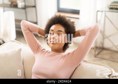 Fröhliche, entspannte, tausendjährige afroamerikanische Frau, die sich auf dem Sofa ausruht, genießen Sie Komfort Stockfoto