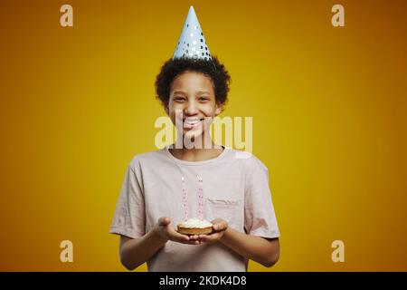 Fröhliches afroamerikanisches Pre-Teen-Mädchen mit einem Stück Geburtstagskuchen mit mehreren brennenden Kerzen, die isoliert vor der Kamera stehen Stockfoto