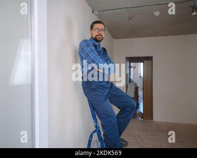 Junger Mann in blau Arbeitsanzug tun Reparatur Wohnung. Renovierungskonzept für das Haus. Stockfoto