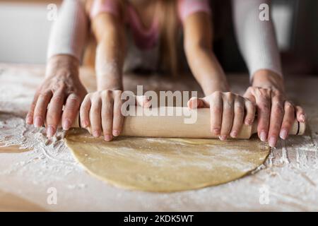 Kaukasische kleine Enkelin und ältere Großmutter, die mit Mehl verschmiert wurde, erzählen Teig mit Nudelholz zum Backen Stockfoto