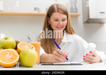 Ein fröhlicher Ernährungsberater schreibt einen Plan für die Einnahme von biologisch aktiven Nahrungsergänzungsmitteln und Vitaminen Stockfoto