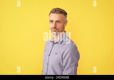 Lächelnder reifer Mann mit grauer Frisur auf gelbem Hintergrund, Friseur Stockfoto