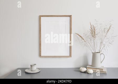 Herbstfrühstück Stillleben Szene. Keramik-Kanne mit trockenem Gras, Tasse Kaffee. Weiße kleine Kürbisse, grauer Tisch. Leeres Modell mit Holzbildrahmen Stockfoto