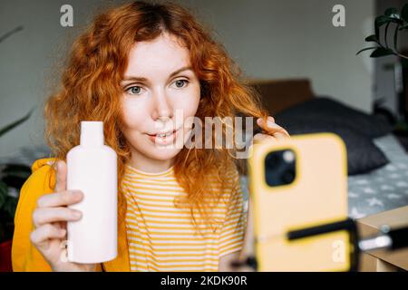 Rothaarige Bloggerin sendet Live-Bewertungen von Schönheitsprodukten für Haare Stockfoto