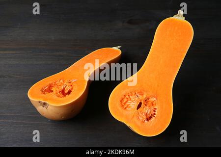 Reife Butternut Squash in der Mitte geschnitten zeigt lebendige Orange Fleisch Isoliert auf schwarzem Holztisch Stockfoto