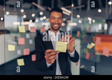 Afrikanischer Geschäftsmann zeigt Haftnotizen mit motivierenden Phrasen, während er im Büro steht Stockfoto