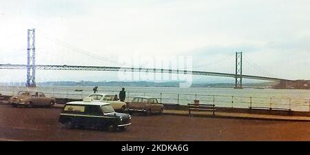 Eine alte Momentaufnahme fotografierte alte Fahrzeuge, die in der Nähe der vierten Straßenbrücke bei South Queensferry geparkt waren, kurz nach ihrer Öffnung für den Verkehr im Jahr 1964, als es die längste Hängebrücke der Welt außerhalb der Vereinigten Staaten war, ursprünglich eine Mautbrücke, aber die Mautgebühren wurden 2008 aufgegeben Stockfoto