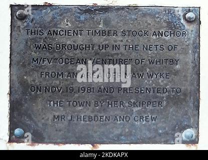 Plakette am Tate Hill Pier, Whitby, Yorkshire, neben einem Anker. Dieser alte Holzlageranker wurde am 19.. November 1981 in den Netzen des Ocean Venture von Whitby aus einem Gebiet vor Maw Wyke aufgezogen und der Stadt von ihrem Skipper J. Hebden und der Besatzung überreicht. Stockfoto