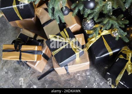 Weihnachtsgeschenke in Gold und Schwarz unter dem Baum verpackt Stockfoto