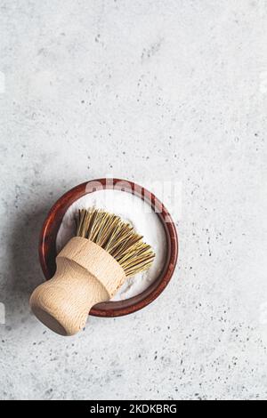 Umweltfreundliches, plastikfreies Hausreinigungskonzept. Soda in Holzschale und natürliche Borstenbürste, grauer Hintergrund, Kopierraum. Stockfoto