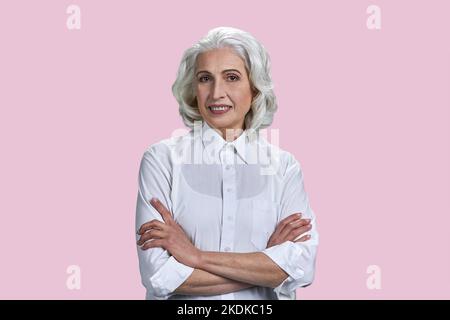 Foto einer alten Rentnerin mit gekreuzten Armen. Isoliert auf rosa Hintergrund. Stockfoto