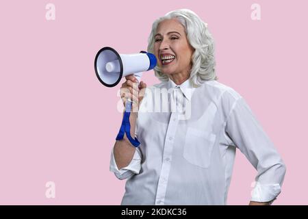 Porträt einer lachenden älteren Frau mit Megaphon. Isoliert auf rosa Hintergrund. Stockfoto