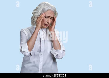 Ältere Frau, die unter starken Kopfschmerzen leidet. Isoliert auf blau. Stockfoto
