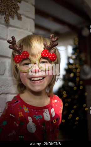 Lächelndes, fröhliches Gesicht eines Kindes in festlicher Schminke eines Hirsches und einer Brille mit Hörnern. Das Kind wartet auf ein Wunder. Weihnachten, Neujahr, fröhliches Wint Stockfoto