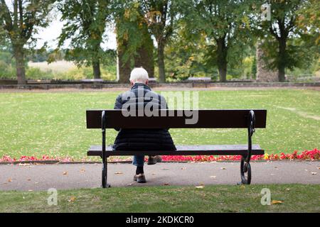 KNARESBOROUGH, Großbritannien - 20. September 2022. Älterer Mann mit grauen Haaren sitzt allein auf einer Parkbank im Herbst. Knaresborough, Yorkshire, Großbritannien Stockfoto