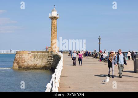 WHITBY, Großbritannien - 21. September 2022. Touristen laufen entlang Whitby Pier (Hafenmauer) mit einem Leuchtturm im Hintergrund. Whitby, North Yorkshire, Großbritannien Stockfoto