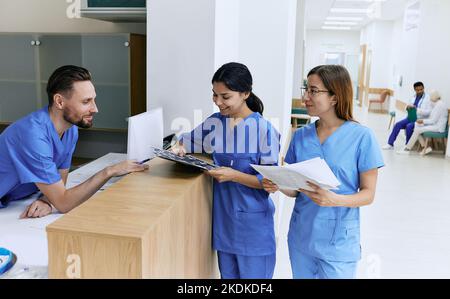 Medizinisches Personal. Medizinische Assistentin im Dienst, die mit weiblichen Krankenschwestern während der Arbeit im Krankenhaus in der Nähe der Rezeption in der Lobby steht Stockfoto