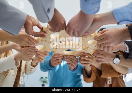 Menschen halten verschiedene hölzerne Zahnräder als Symbol für Einheit, Unterstützung und gemeinsame Ziele. Stockfoto