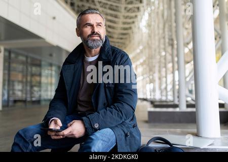 Erwachsener bärtiger Geschäftsmann, der im Flughafengebäude auf das Einsteigen in ein Flugzeug wartet Stockfoto