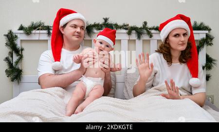 Frau weigert sich, sich um das Baby auf dem Bett zu kümmern, das für weihnachten und Neujahr dekoriert ist, Familienpaar im Schlafzimmer zu Hause Stockfoto