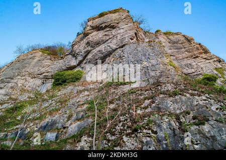 Hohe Kalksteinfelsen, teilweise bebaut, mit Höhleneingängen und künstlichen Eingängen für Bleiminen, in Middleton Dale, Stoney Middleton, Peak District. Stockfoto