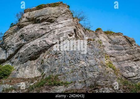 Hohe Kalksteinfelsen, teilweise bebaut, mit Höhleneingängen und künstlichen Eingängen für Bleiminen, in Middleton Dale, Stoney Middleton, Peak District. Stockfoto