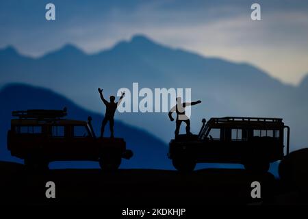 Miniatur-Spielzeuge zweier Männer feiern triumphierend am Bergkonzept. Stockfoto