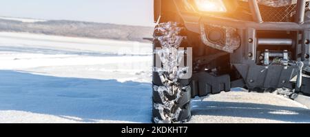 Nahaufnahme des vorderen POV-Nahaufnahme eines Quad-Offroad-Fahrzeugs, das an einem sonnigen, schneebedeckten, kalten Wintermorgen bei klarem, blauem Himmel auf der Snowdrift-Strecke geparkt ist. ATV Stockfoto